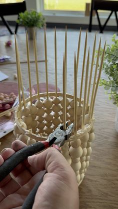 a person is holding a pair of pliers in front of a basket with sticks sticking out of it