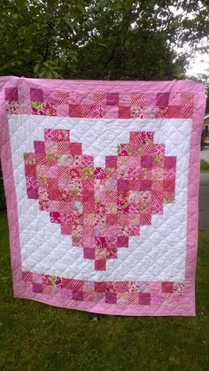 a pink and white heart quilt hanging from a tree