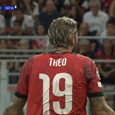 a soccer player with his back turned to the camera and fans in the stands behind him