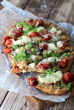 two pizzas with tomatoes, mozzarella and basil on top sitting on wax paper