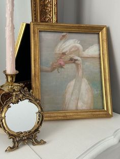 a white swan with pink flowers in its beak next to a mirror and candle holder