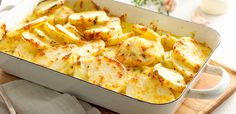 a casserole dish filled with potatoes on top of a wooden cutting board next to silverware