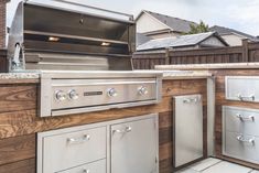 an outdoor kitchen with stainless steel appliances and wood clad cabinets on the side of it