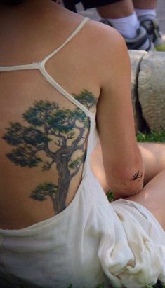 a woman sitting in the grass with a tattoo on her back