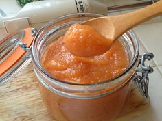 a wooden spoon in a glass jar filled with orange colored sauce on top of a cutting board