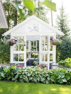 a small white house with lots of windows and plants in the front yard, surrounded by greenery