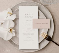 a table setting with white flowers and menu cards on it, along with silverware