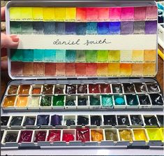 a box filled with lots of different colored watercolors next to a person's hand