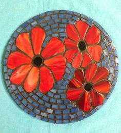 an orange and blue mosaic with flowers on it's side, sitting on a turquoise surface