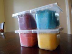 three plastic containers with different colored food in them sitting on a wooden table next to a wall