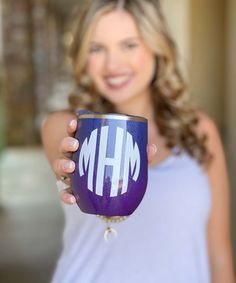 a woman holding up a purple and white coffee cup with the letter h on it