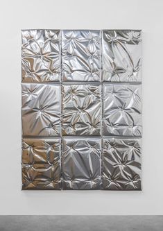 an abstract piece of art made out of aluminum foil on a wall in a white room