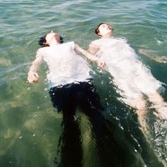 two people are floating in the water on their stomachs and one person is wearing a white shirt