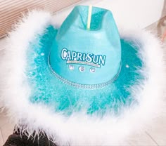 a turquoise cap with white feathers on it sitting on top of a table next to a window