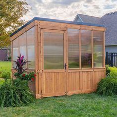 a small wooden greenhouse in the middle of a yard with flowers and plants around it