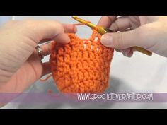 two hands crocheting the ends of an orange knitted object with a yellow knitting needle