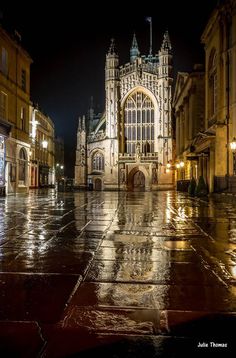 an image of a city street at night with rain on the ground and buildings in the background