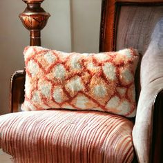 an orange and white pillow sitting on top of a brown chair next to a lamp