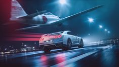 a sports car driving down the road in front of an airplane at night with bright lights