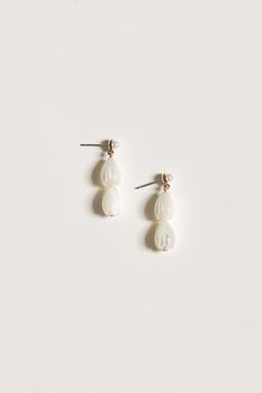 two white pearls are hanging from the back of small silver ear pins on a white surface