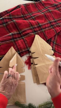 someone cutting out christmas trees with scissors on the ground next to them and wrapping paper