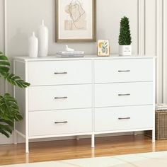 a white dresser sitting in a living room next to a potted plant