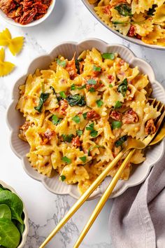 two bowls filled with pasta and spinach on top of a white table next to some yellow chopsticks