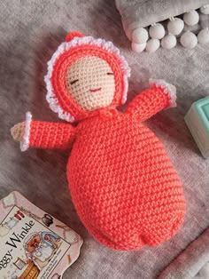 a crocheted doll laying on top of a bed next to a book and toy