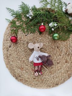 a small stuffed mouse is sitting on a mat with christmas ornaments and greenery in the background