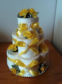 a three tiered wedding cake with yellow flowers and ribbons on the top, sitting on a wooden table