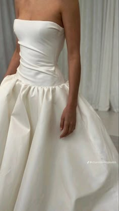 a woman in a white wedding dress with her hand on the back of her skirt