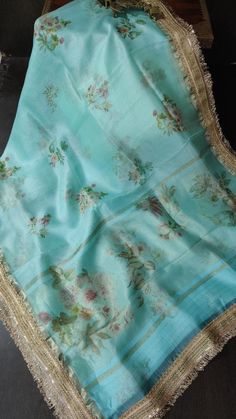 Make a stunning statement with this Teal Pure Organza Silk Saree, beautifully adorned with a vibrant floral digital print that captures the essence of nature. The lightweight organza fabric offers a delicate drape, creating an airy and ethereal silhouette that enhances your elegance. The floral patterns, bursting with rich colors, bring a lively charm to the saree, while the intricate lace trim border adds a touch of sophistication and refinement. Ideal for various occasions, from casual gatherings to festive celebrations, this saree effortlessly combines style and comfort. With its captivating design and luxurious feel, this teal saree is sure to make you stand out in any crowd. Designer Blue Floral Print Dupatta, Summer Digital Print Saree, Spring Floral Print Saree, Elegant Summer Saree With Floral Print, Elegant Floral Print Saree For Summer, Elegant Summer Floral Print Saree, Spring Wedding Saree With Floral Print, Traditional Summer Saree With Digital Print, Traditional Summer Digital Print Saree