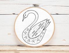 the embroidery pattern shows a swan with an arrow in its beak, on a white wooden background