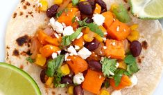 a tortilla topped with black beans, carrots and feta cheese next to a lime wedge