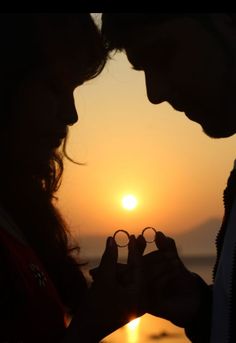 two people standing next to each other with the sun setting behind them