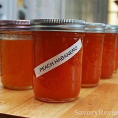 four jars filled with peach jam sitting on top of a wooden table next to each other