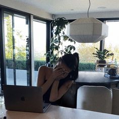 a woman sitting in front of a laptop computer on top of a table next to a plant