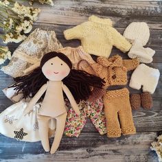 an assortment of knitted dolls and clothing laid out on a wooden table with dried flowers