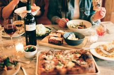 people sitting at a table with food and wine in front of them, eating pizza