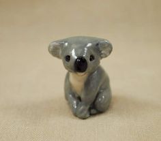 a small grey koala figurine sitting on a beige surface with black eyes