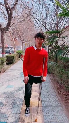 a man in red sweater and black pants walking with crutches on sidewalk next to trees