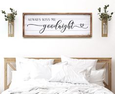 a bed with white sheets and pillows in front of a wooden sign that says always kiss me goodnight