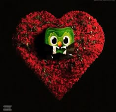 a heart shaped object with a green monster face on it's side and red flowers in the shape of a heart