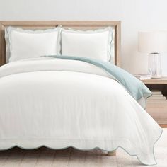 a bed with white sheets and pillows in a room next to a lamp on a table