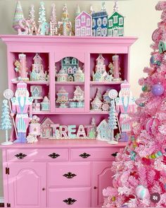 a pink christmas tree in front of a pink china cabinet with lots of decorations on it