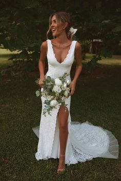 a woman in a white wedding dress holding a flower bouquet and posing for the camera