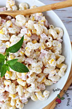 a white bowl filled with macaroni salad next to two wooden spoons on top of a table