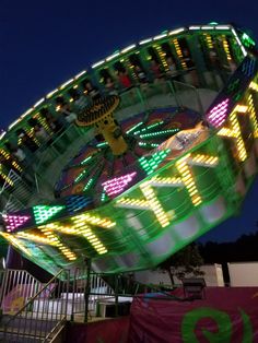 an illuminated carnival ride at night with people riding on the top and below it's lights