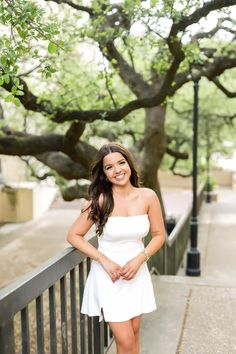 a beautiful young woman posing for a photo in front of a tree with her hands on her hips