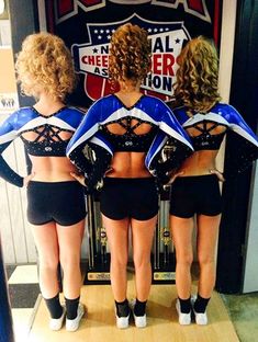 three women in black and blue cheerleader outfits are looking at their reflection in a mirror